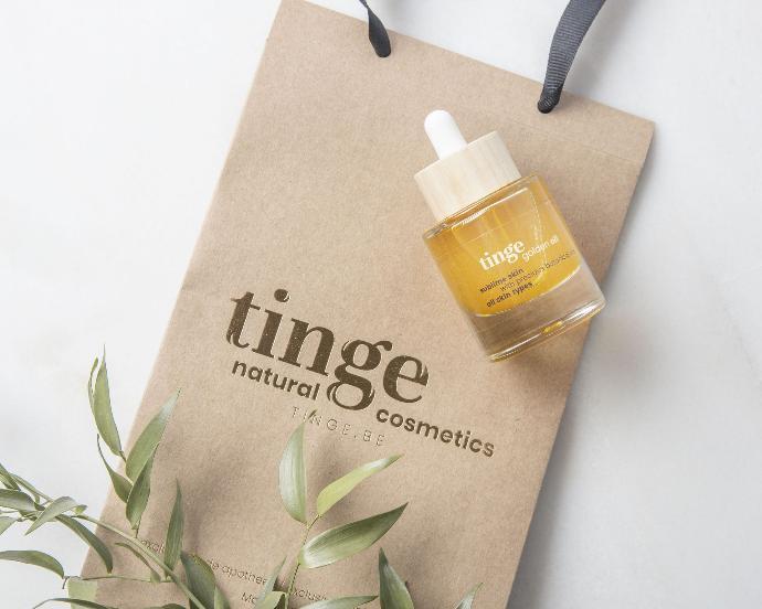 tinge natural cosmetics bag with golden oil bottle on top