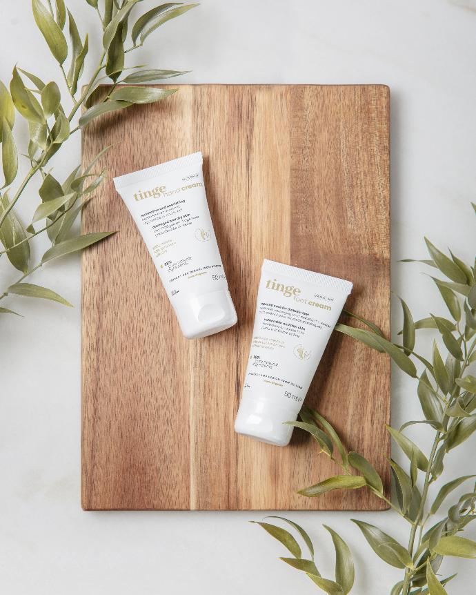 Tinge pampering package for hands and feet tinge pampering package for hands and feet tube on a wooden board with plants nearby